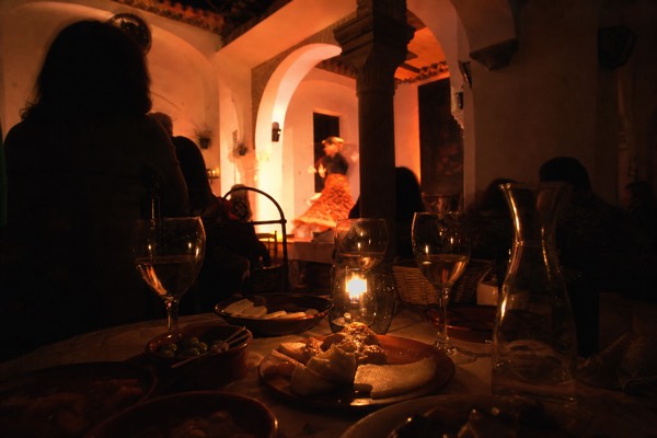 Candlelit dinner table set close to a tablao stage in Seville with tapas and wine glasses