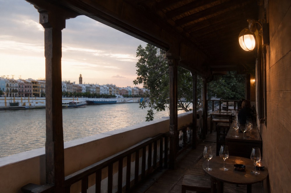 A quiet riverside promenade in Triana in late afternoon light with moored boats and pastel building facades across the water