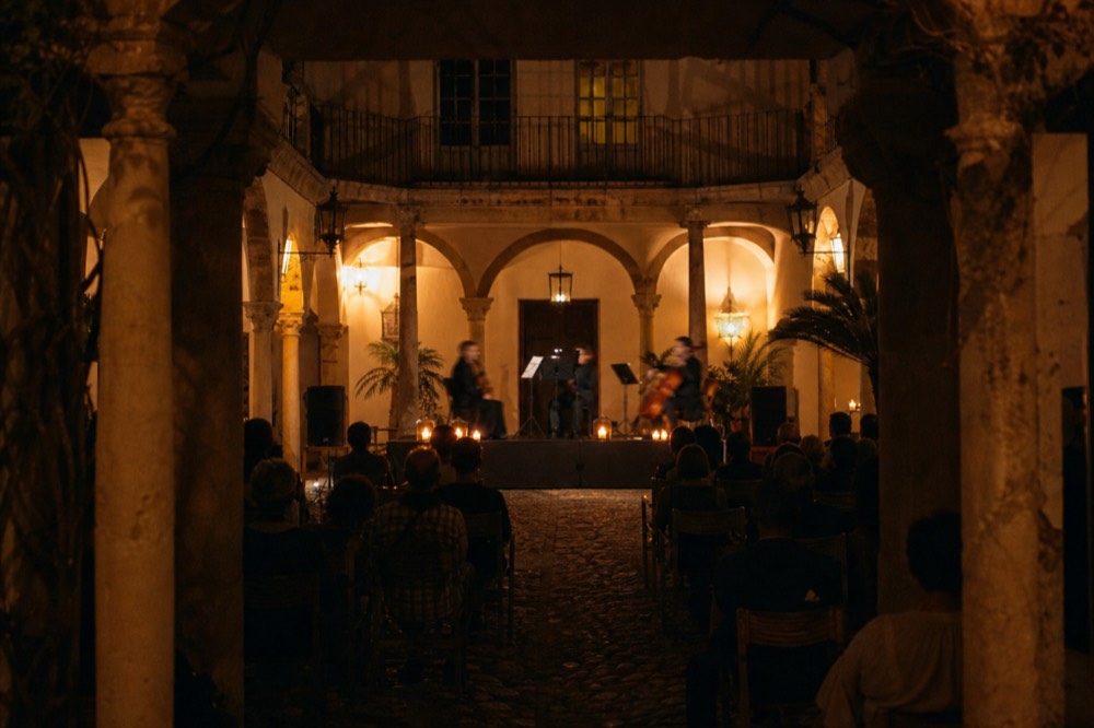 Eighteenth-century Andalusian courtyard at night with stone columns, a small stage in the centre and lantern light on the walls