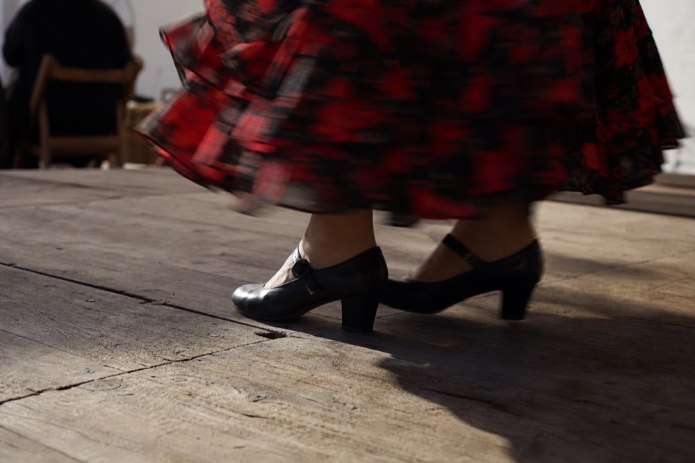 Close view of worn wooden stage boards and a dancer's shoes striking mid-step, motion blur across the hem of the skirt