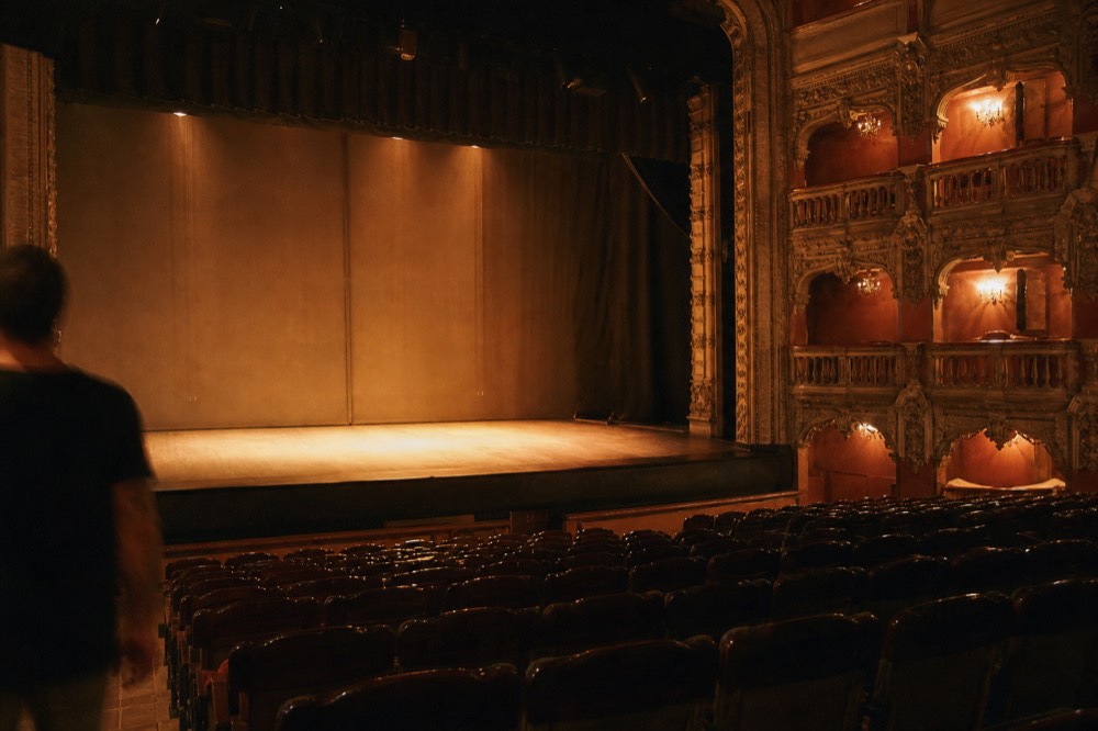 Empty theater seats in a historic Seville auditorium with warm stage lighting and a bare wooden performance floor