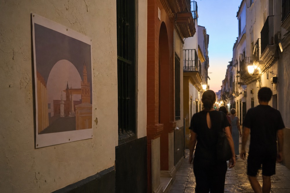 Narrow Seville street in September evening light with a printed programme poster on a wall and people walking past