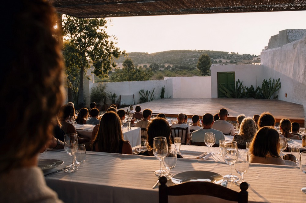 Long dinner tables arranged in tiers facing a bare wooden tablao stage, glasses and cutlery set before the show