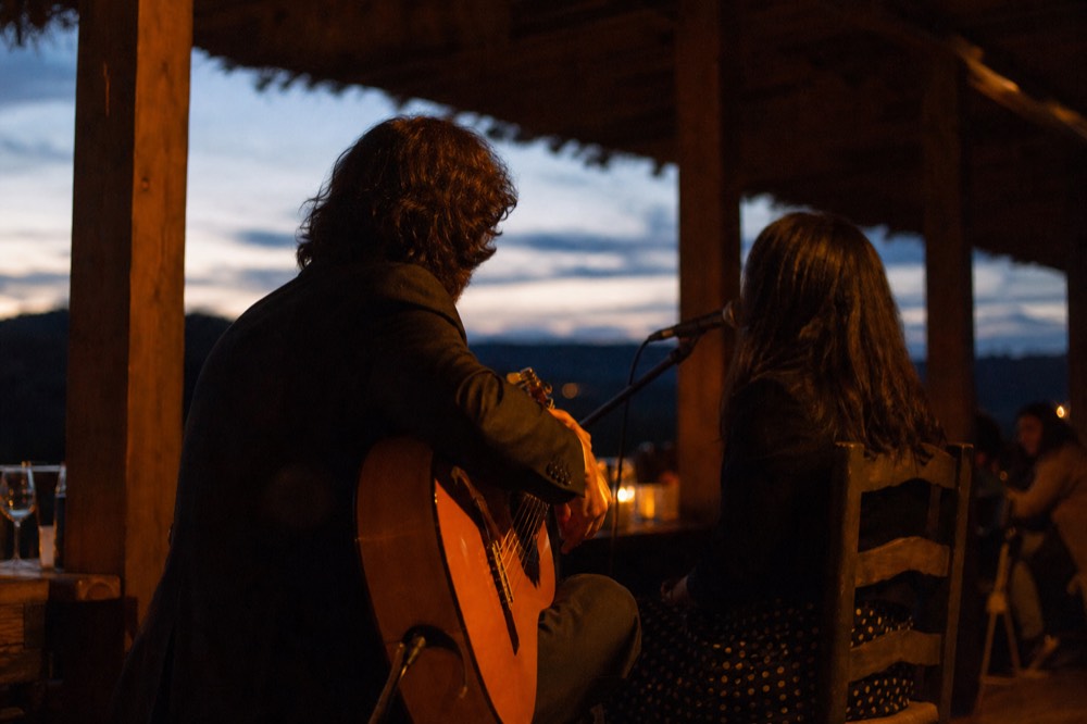 Close view of a guitarist and singer seated side by side on a small stage, faces turned away, warm side light on the guitar