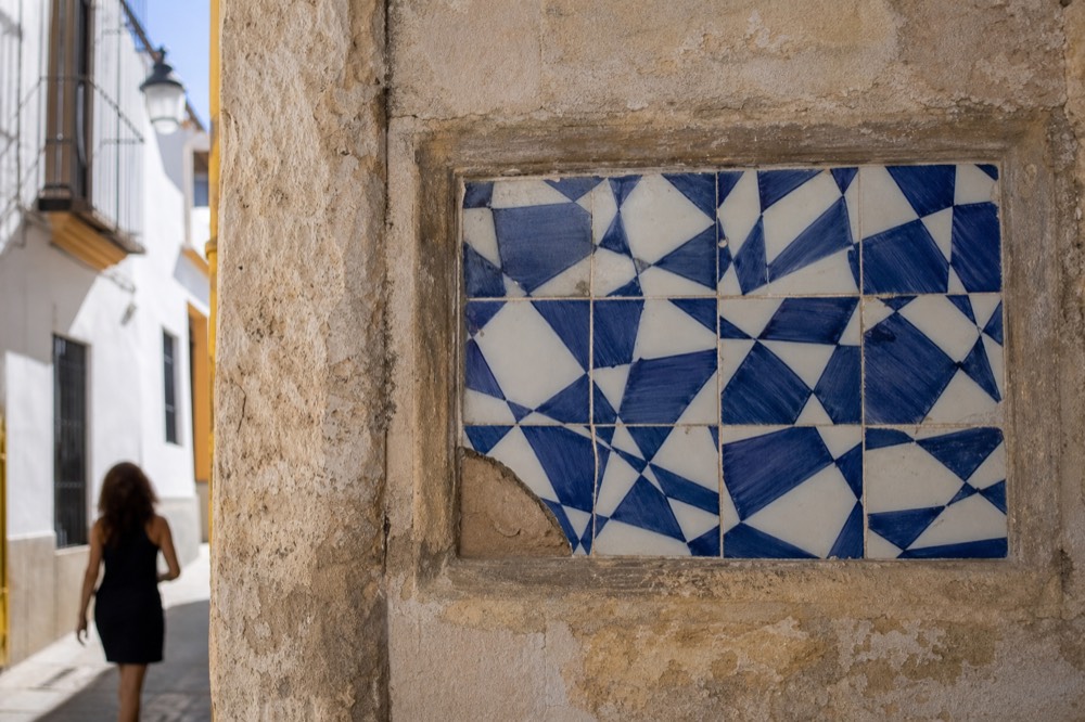 Weathered ceramic tile panel set into an old Triana wall, geometric blue and white pattern, chipped at one corner
