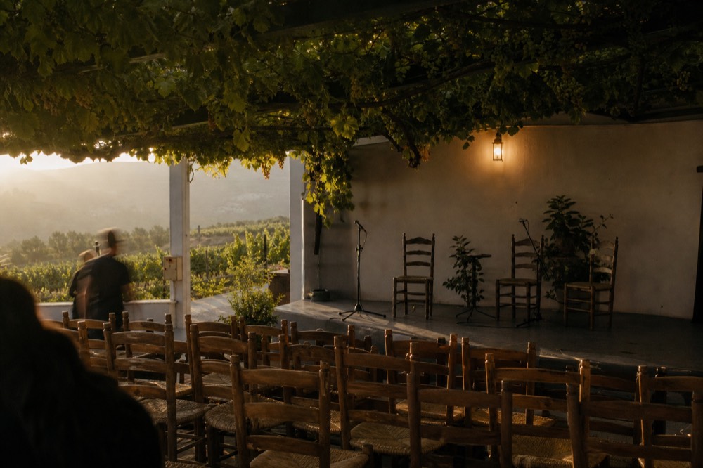 Row of empty wooden chairs facing a small tablao stage lit by a single warm lamp before the audience arrives