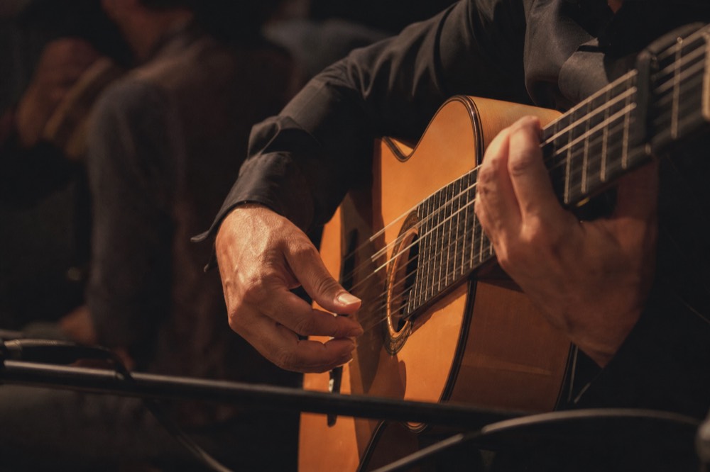 Flamenco guitarist's hands on the strings in close view, the rest of the darkened stage out of focus behind