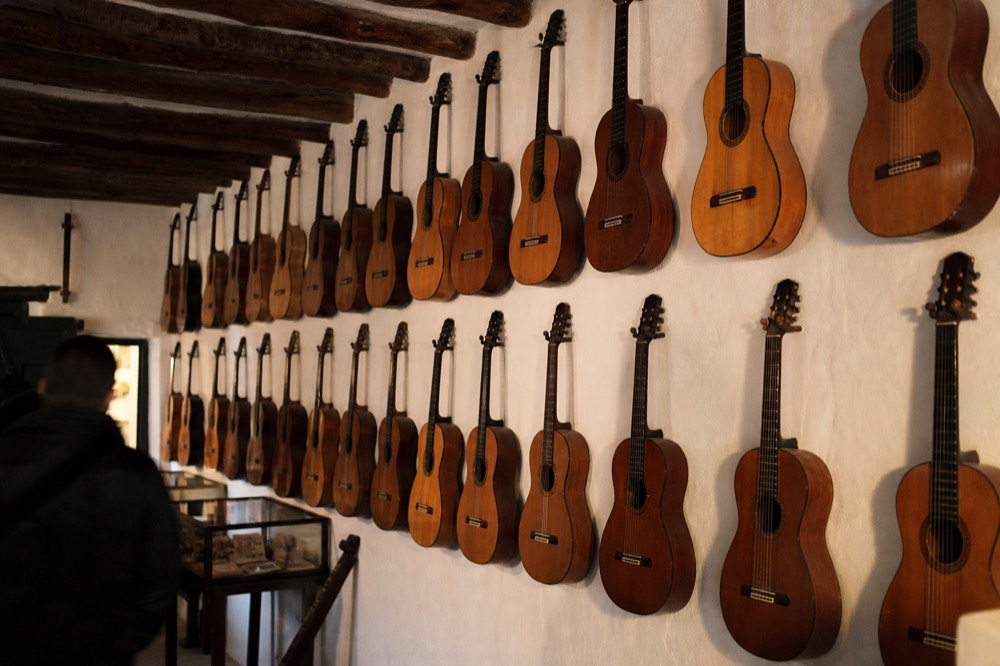 Wall of historic flamenco guitars hanging in a small whitewashed exhibition room with wooden ceiling beams