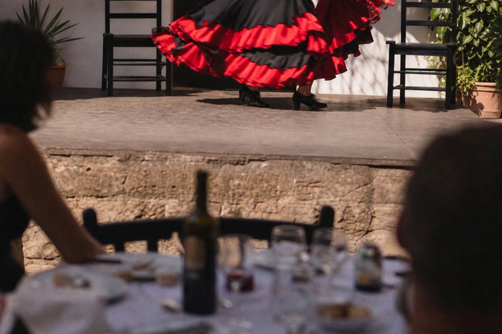 Dinner table set beside a low flamenco stage with a dancer's skirt caught mid-turn in the background