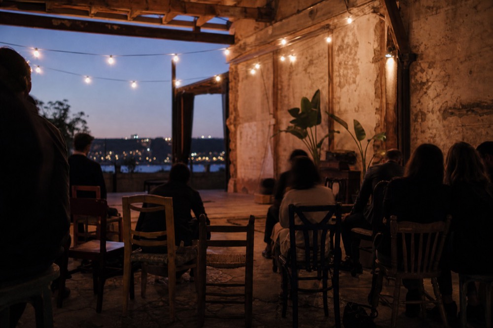 Rough plastered wall and open wooden beams of a converted coal yard bar in Seville, mismatched chairs pulled toward a small clear floor