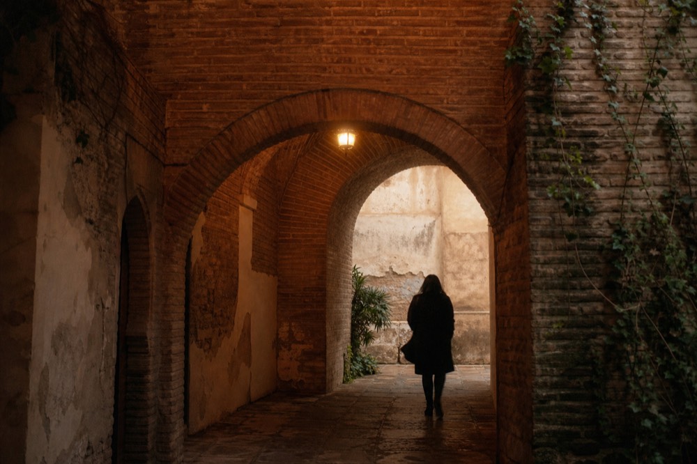 Ancient brick arch and vaulted ceiling lit by a single lamp, worn stone floor below, no furniture in the frame