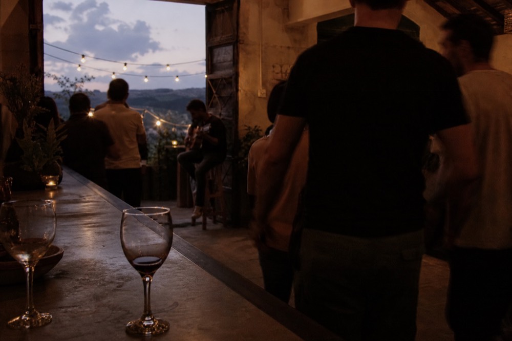 Crowded rustic Seville bar with a guitarist playing on a stool in the corner, standing drinkers in the foreground, glasses on a zinc counter