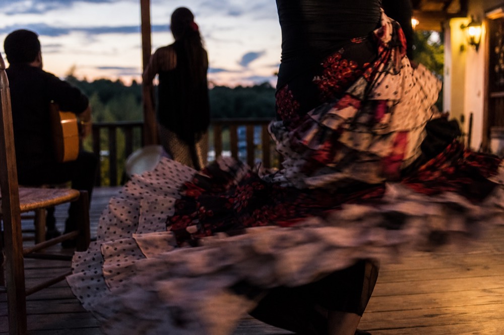 Close crop of a flamenco dancer's long trained dress sweeping across a wooden stage floor, ruffles blurred with movement