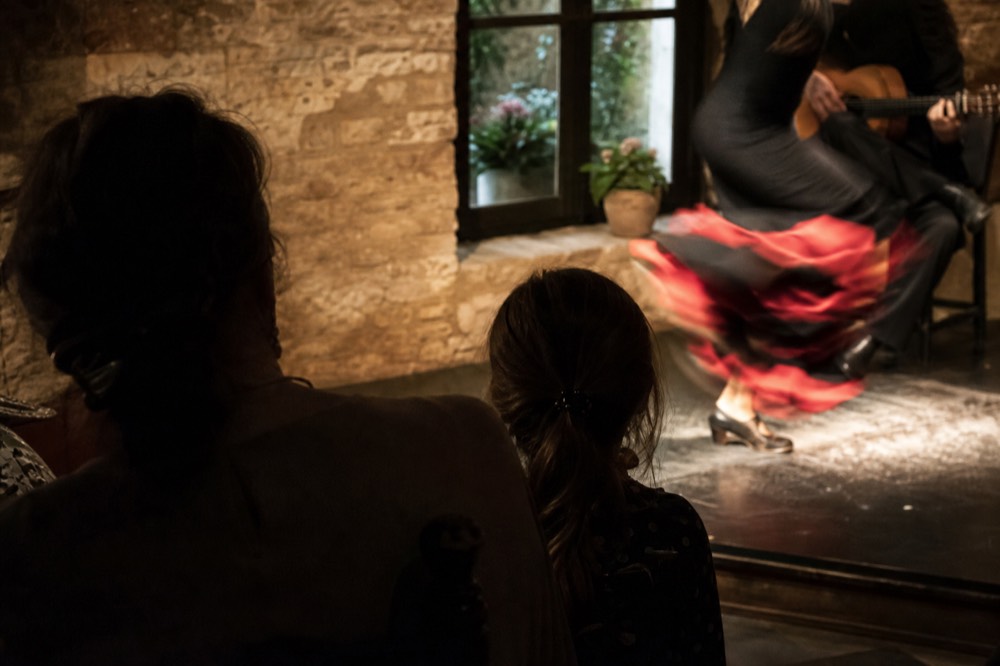 Child sitting with a parent in a front row at an early flamenco show, both watching a dancer whose feet are blurred in motion